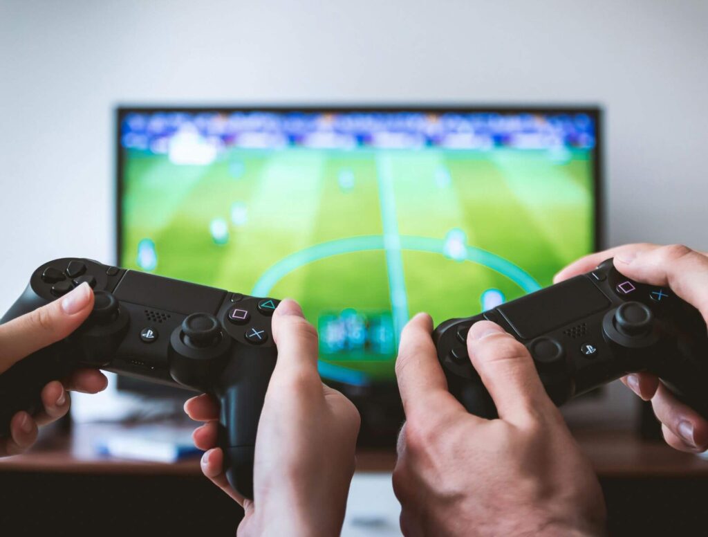 two sets of hands holding video game controllers with tv in background